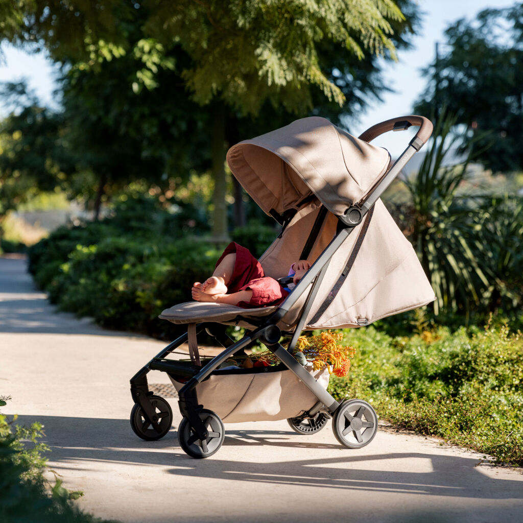 A child relaxes in the Joolz Aer2 stroller with the sun canopy fully extended while parked on a tree-lined path in a sunny park.